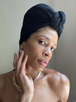 Woman with a black headscarf/towel adjusting applying Primally Pure Serum onto face a neutral background