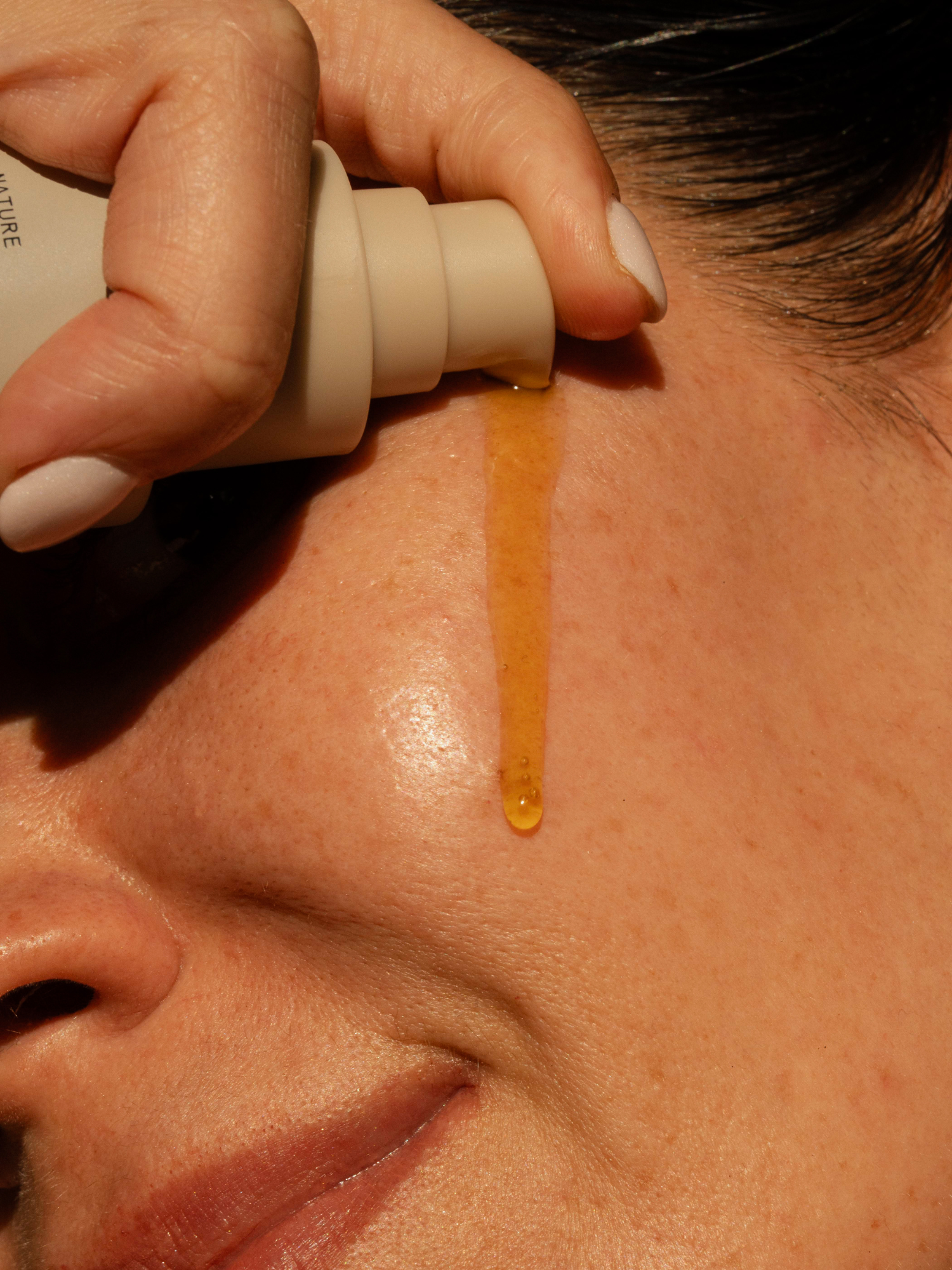 Close-up of a hand applying Primally Pure Regenerative Hemp Serum to a woman's face.