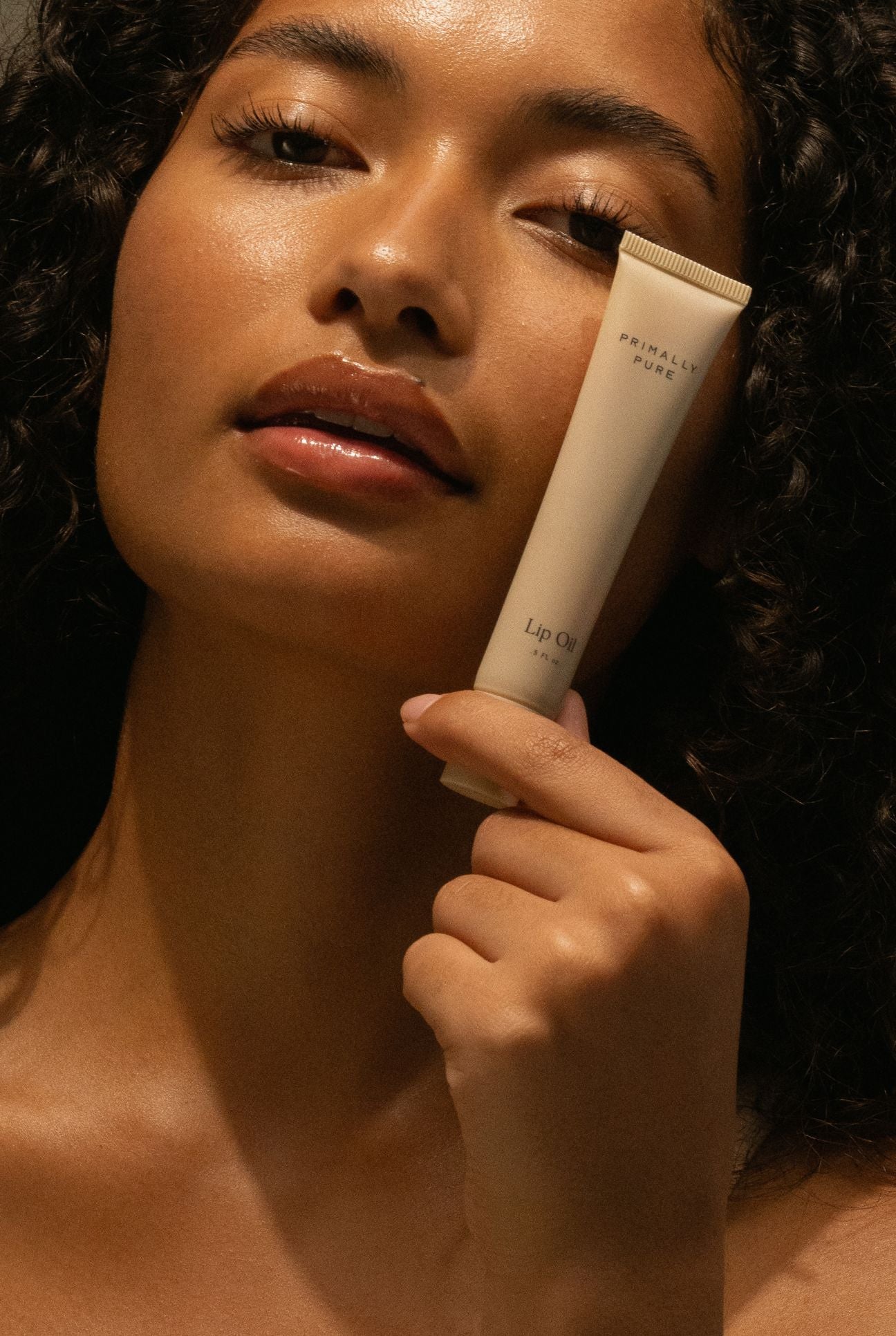 Woman holding a tube of Primally Pure lip oil close to her lips. Primally Pure Lip Oil  on models lips glossy non-toxic lip care
