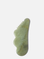 Green gua sha stone with a unique shape, designed for facial and body massage to promote circulation and reduce tension.