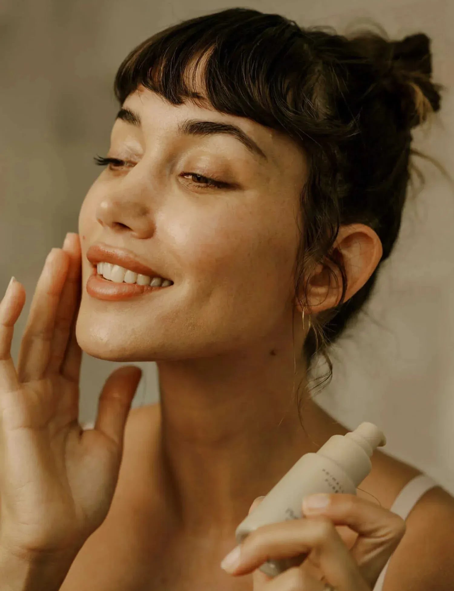 Woman applying Primally Pure Plumping Serum product to her face with a neutral background