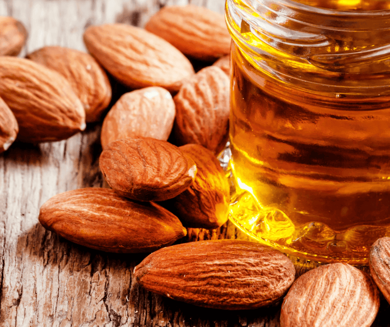 Almonds and a bottle of almond extract oil on a wooden surface.