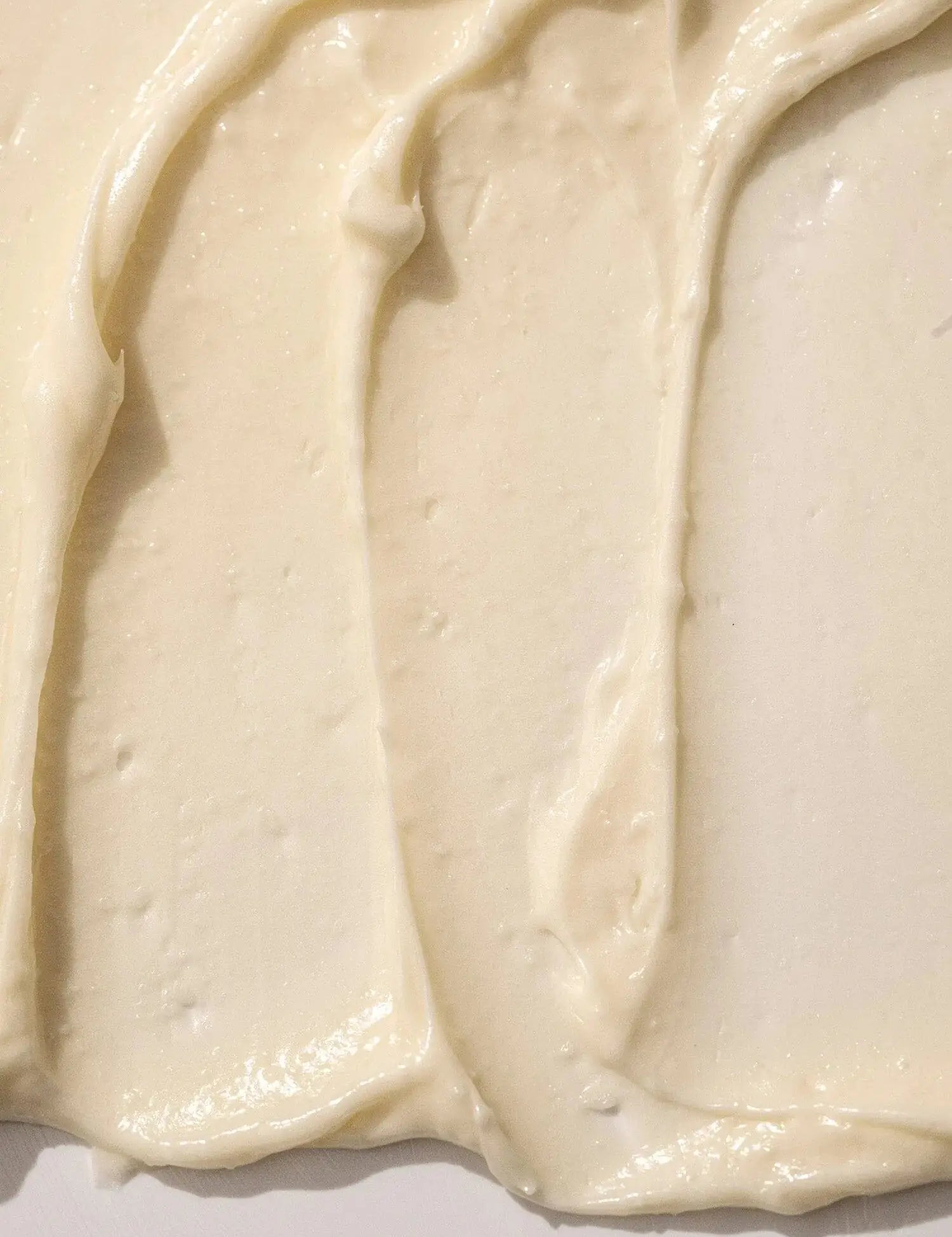 Person holding a green jar of Almond + Vanilla body butter using their other had to apply the body butter to their leg against a neutral background