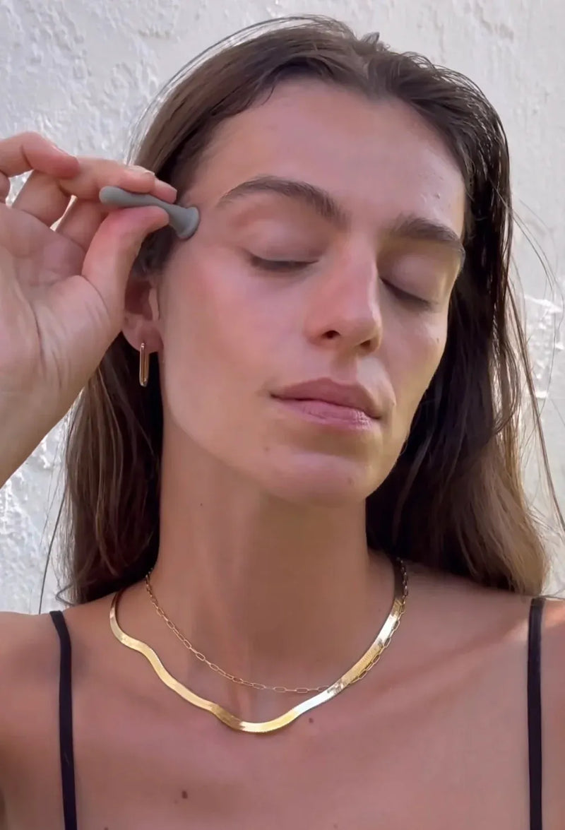 Woman using Primally Pure Facial Cupping Tool on her face around eye area against a neutral background