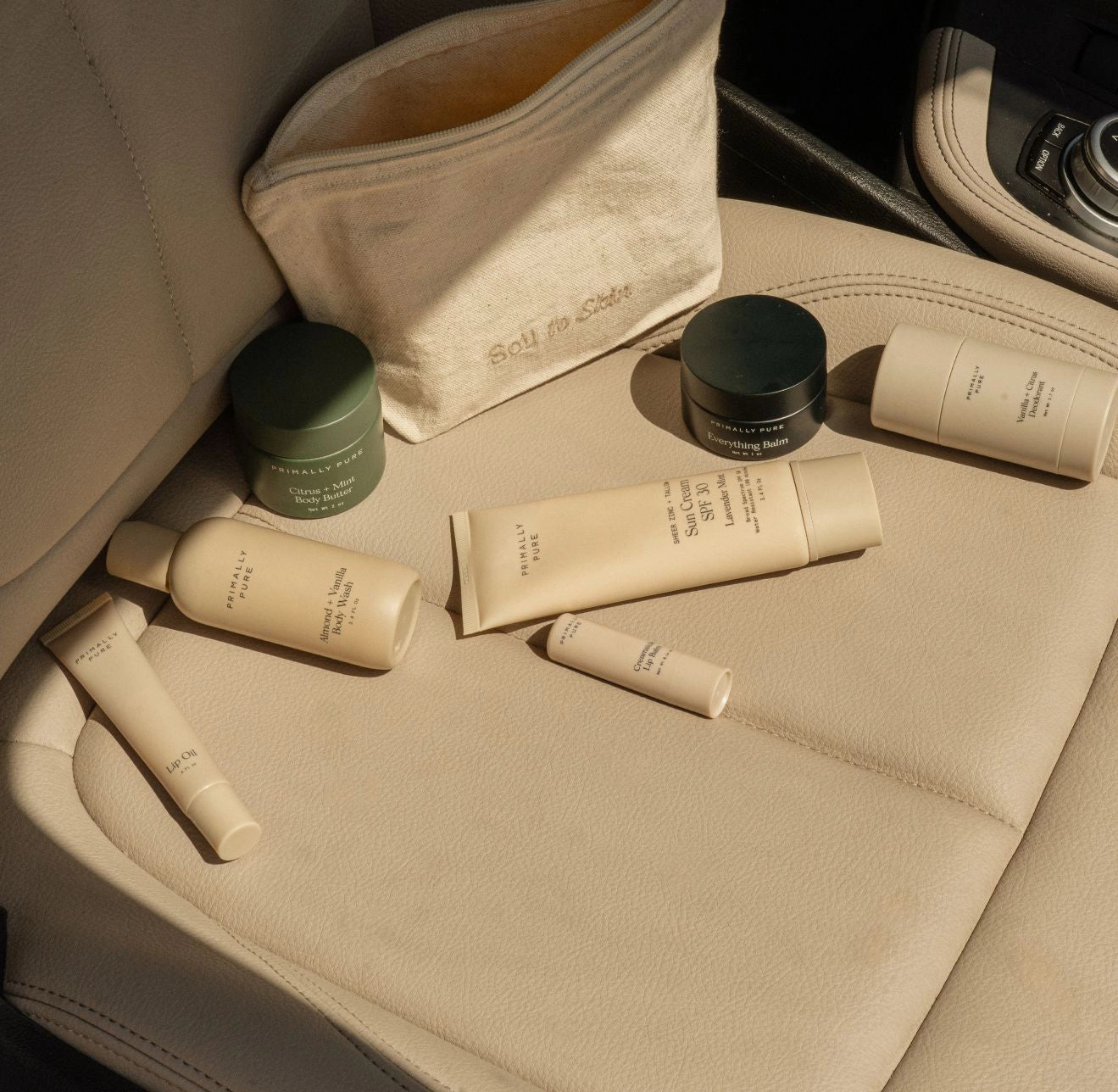Primally Pure Skincare products on a car seat with a beige "Soil to Skin" organic cotton skincare pouch. Non-Toxic Skincare and Wellness Products for the whole family this Back-To-School season