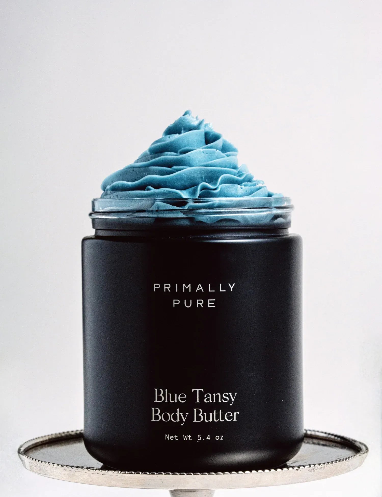 Black Jar of Primally Pure Blue Tansy on a white background showing the butter-like texture of Blue Tansy Body Butter