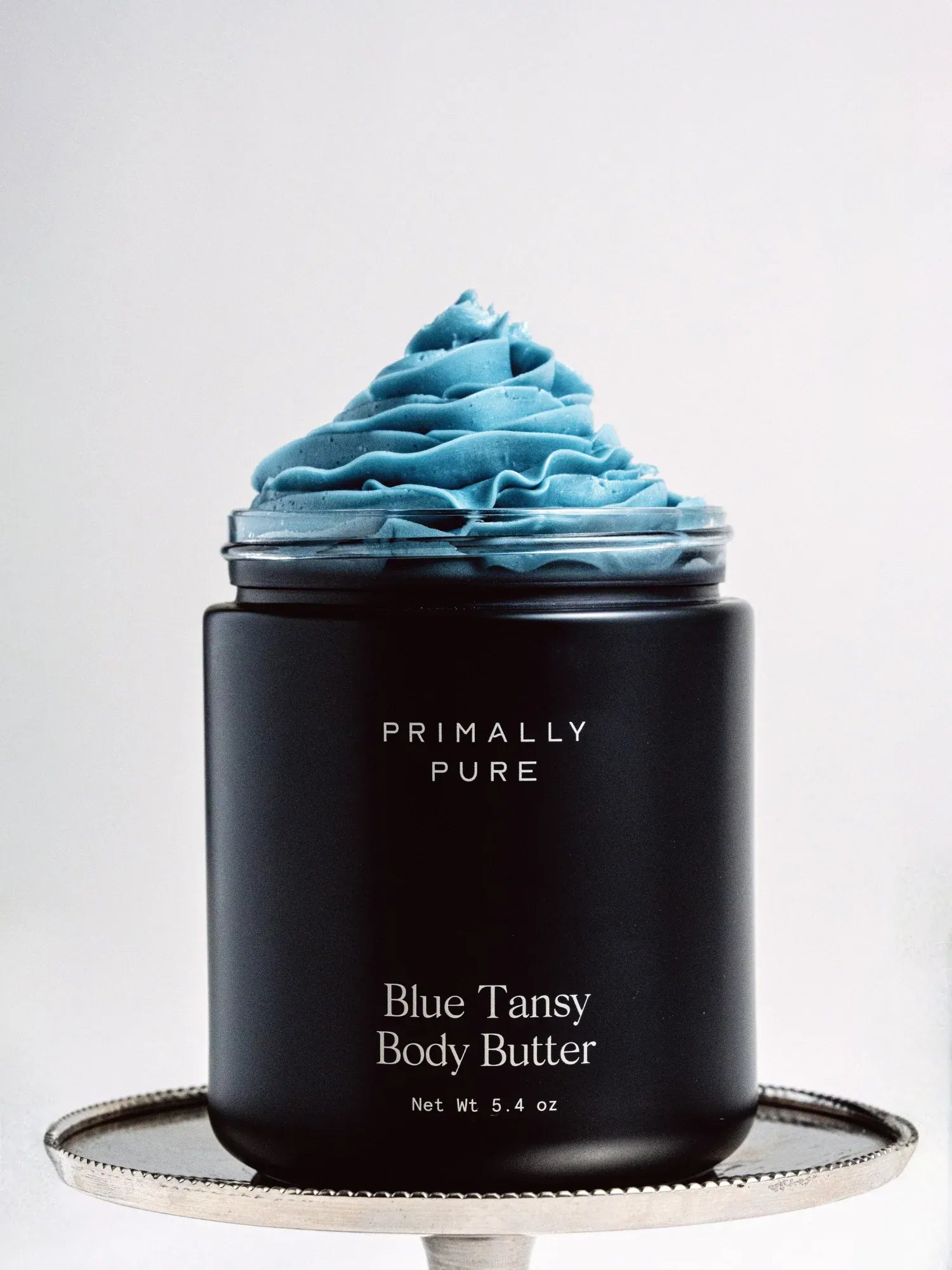 Black Jar of Primally Pure Blue Tansy on a white background showing the butter-like texture of Blue Tansy Body Butter