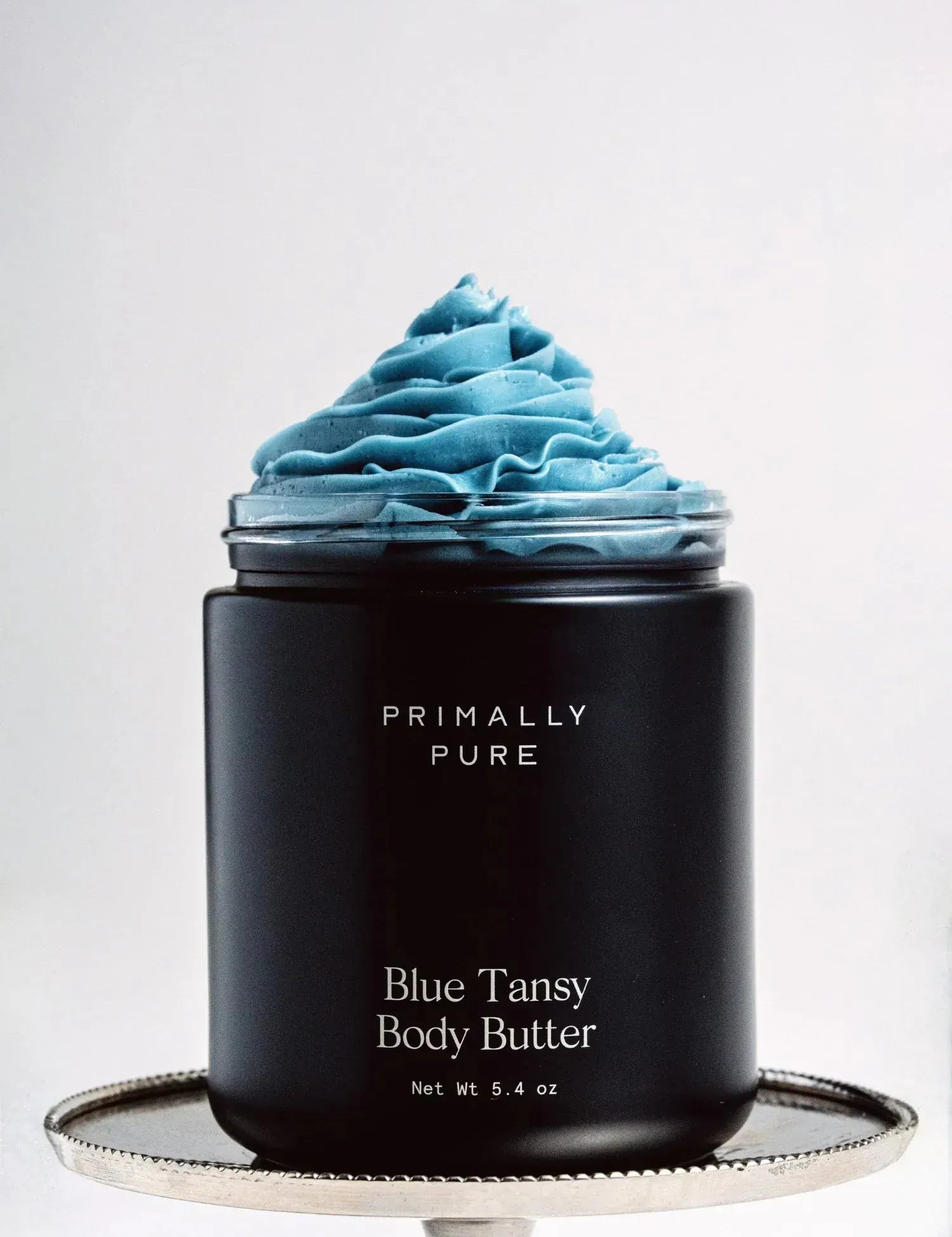 Black Jar of Primally Pure Blue Tansy on a white background showing the butter-like texture of Blue Tansy Body Butter