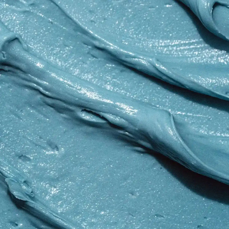 A close-up texture shot of a thick, creamy  Blue Tansy Body Butter - a dusty light blue color, showing swirled folds and a glossy, slightly sparkly finish.