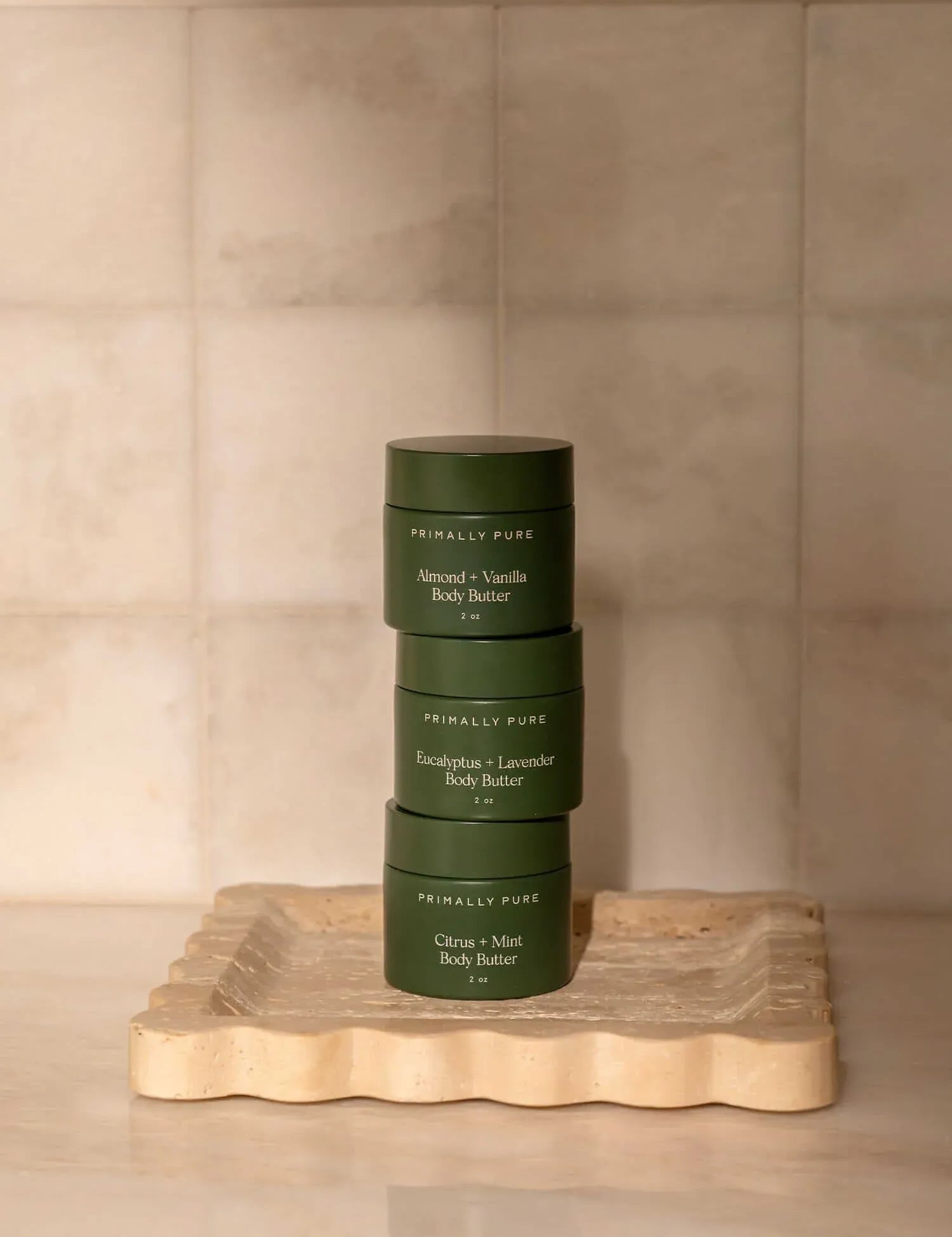 Stack of mini body butter trio products on a wooden tray with a beige background