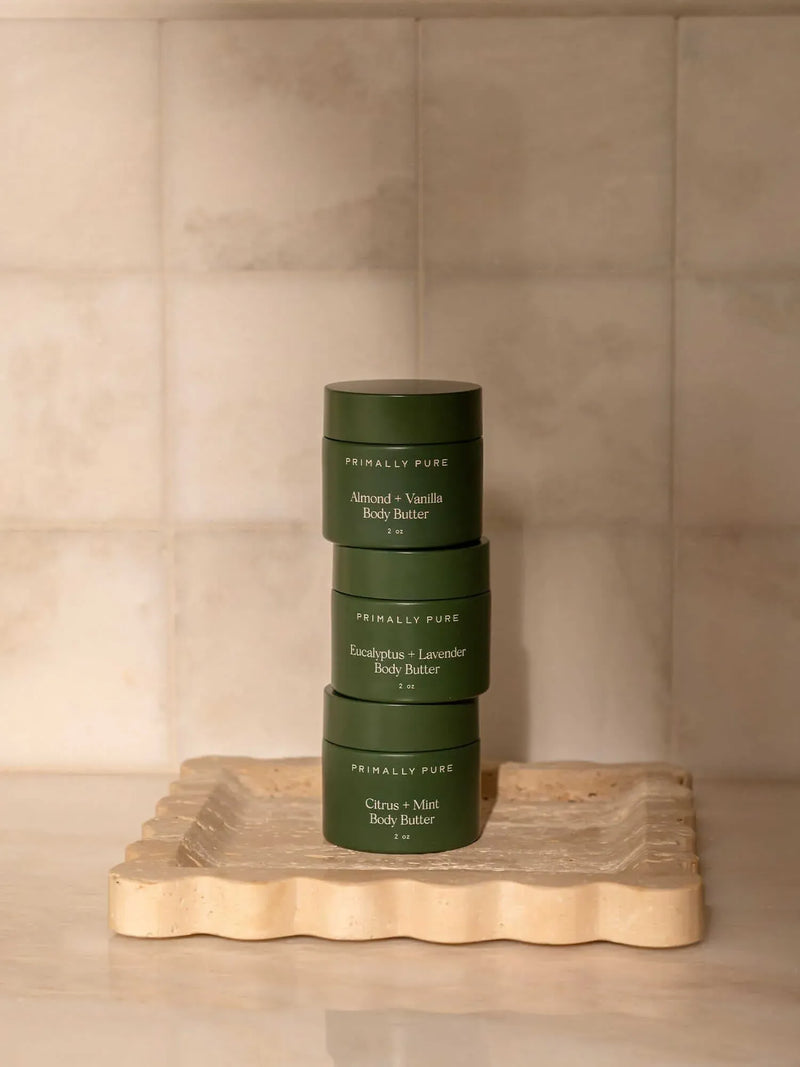Stack of mini body butter trio products on a wooden tray with a beige background