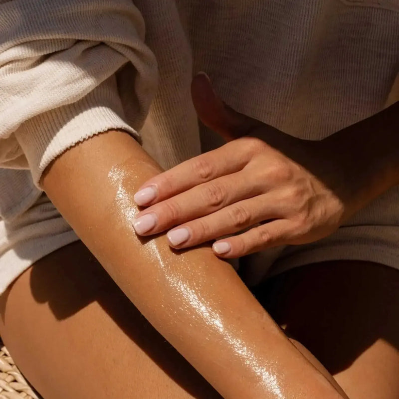 Close-up of a person applying Body Butter onto their forearm, wearing a ribbed light beige sweatshirt.