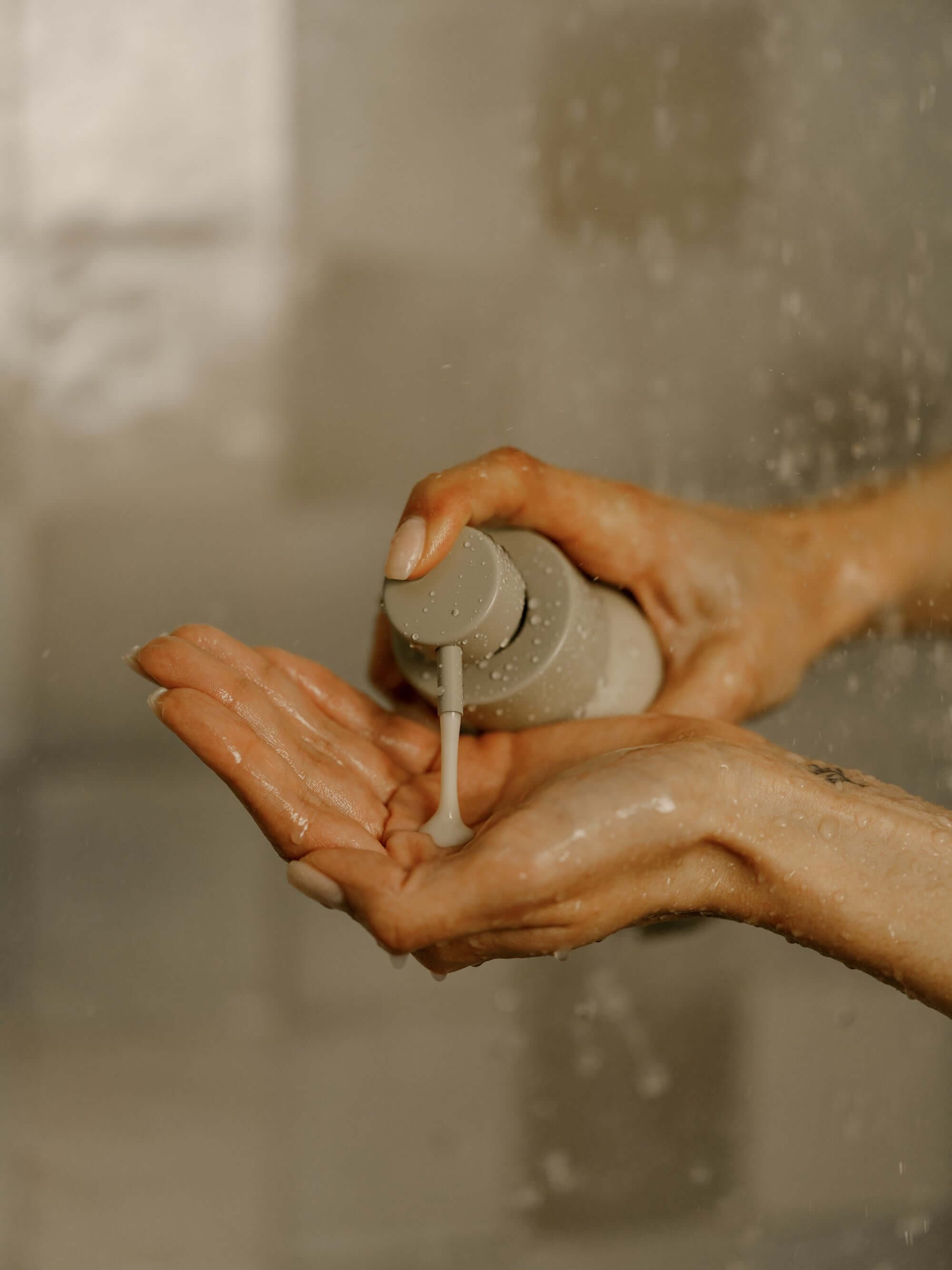 Person applying Primally Pure Body Wash from a bottle in a shower setting
