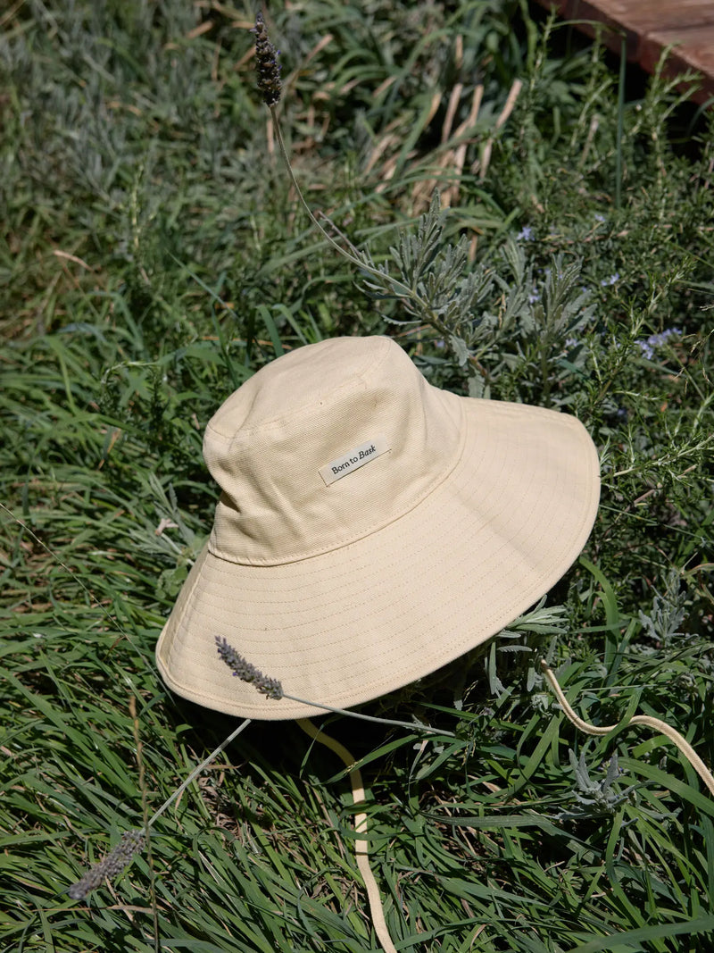 A beige wide-brim sun hat resting on green grass outdoors. A small woven label on the crown reads 'Brixton Bad' or similar, but the text is too small to confidently identify as a visible brand, so I leave brands empty.