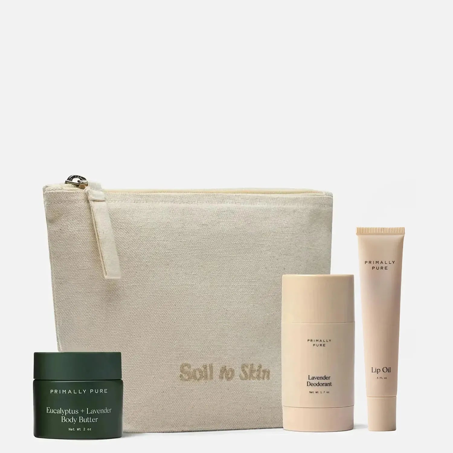 A skincare set from Primally Pure on a light gray background, featuring a beige canvas pouch with 'Soil to Skin' printed on it, a dark green eucalyptus + lavender body butter jar, a beige lavender deodorant stick, and a beige lip oil tube.