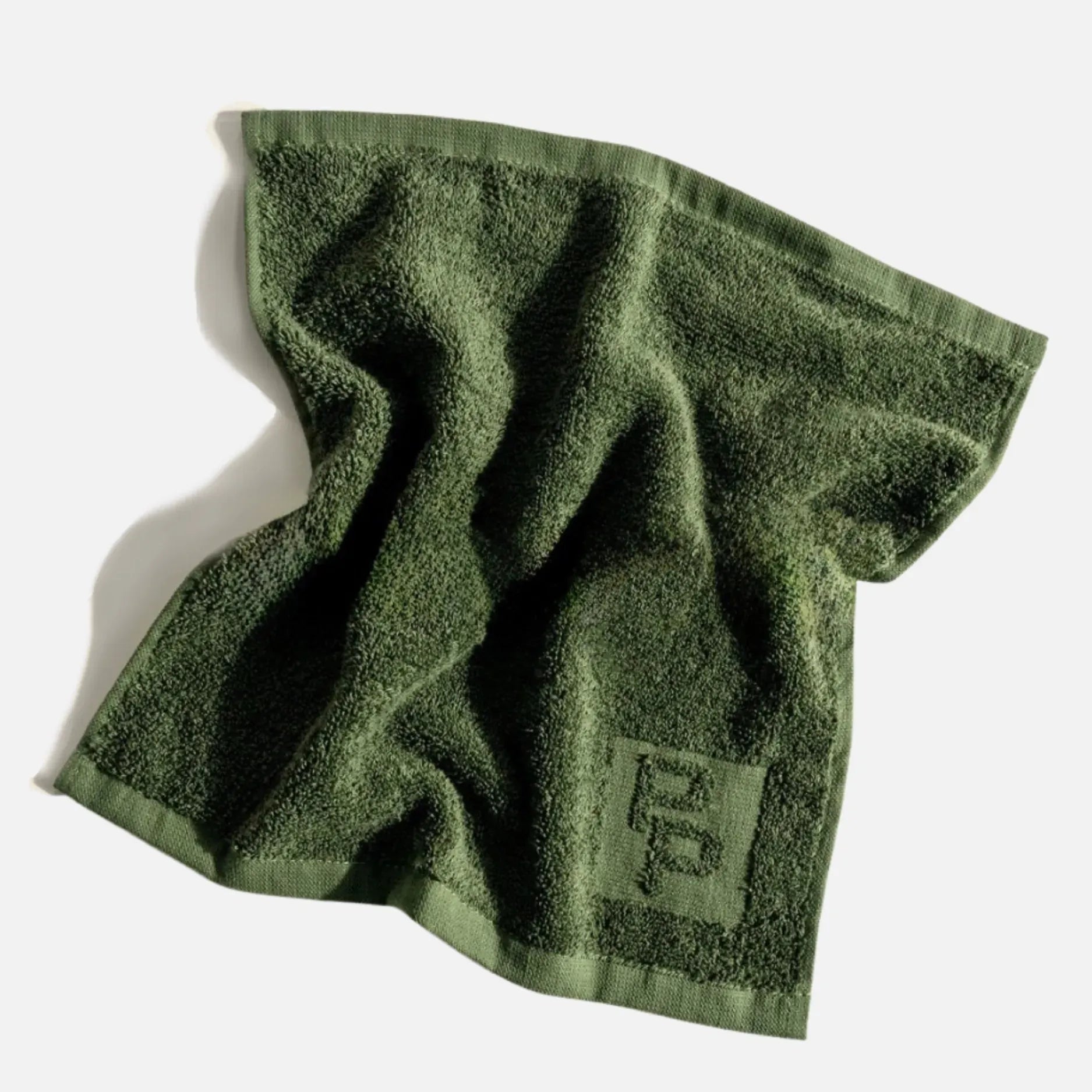 A green cleansing cloth face towel featuring an interlocking 'P' for Primally Pure logo, shown on a clean white background with a soft shadow.