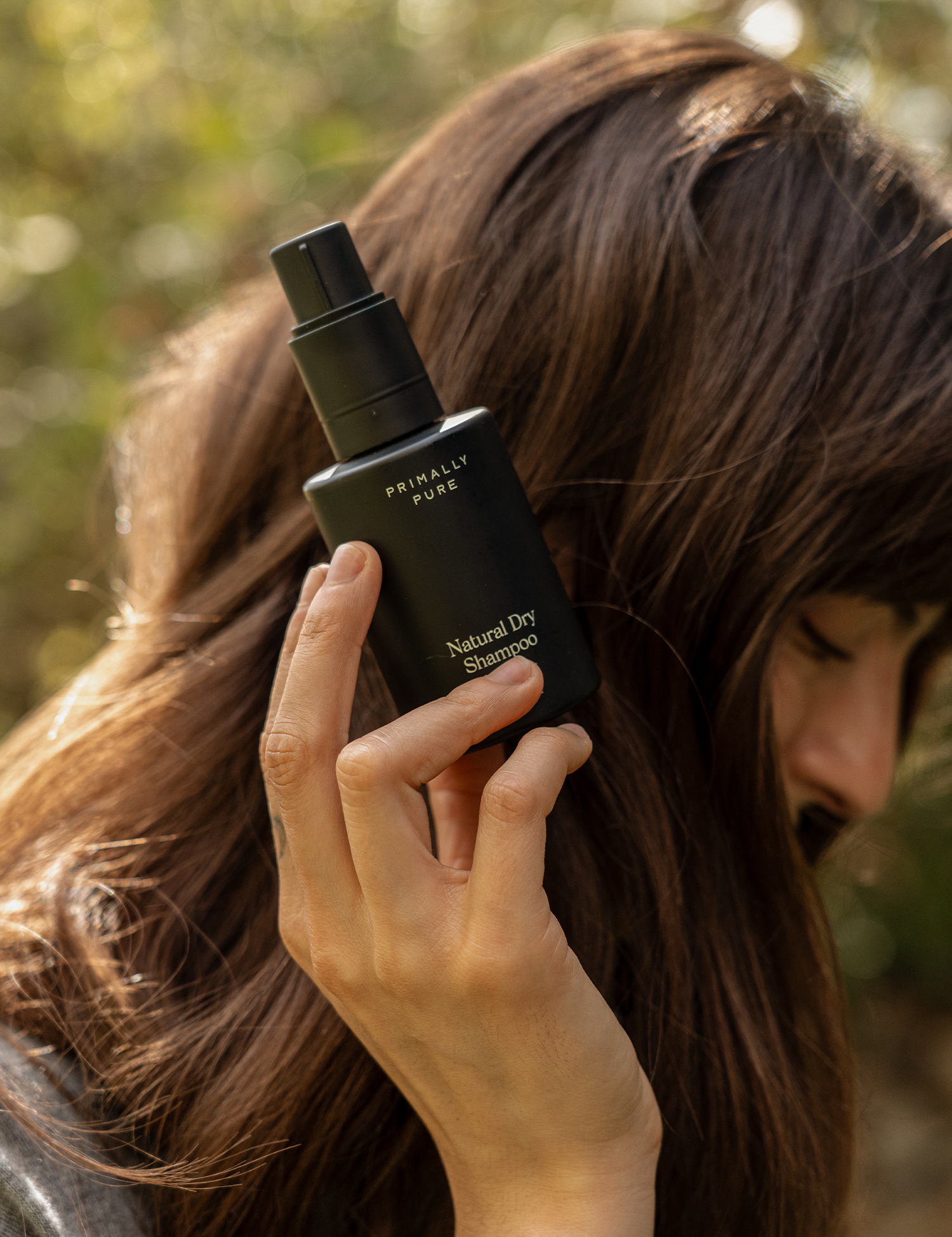 Person holding Primally Pure Natural Dry Shampoo in a black bottle, designed for refreshing hair naturally.