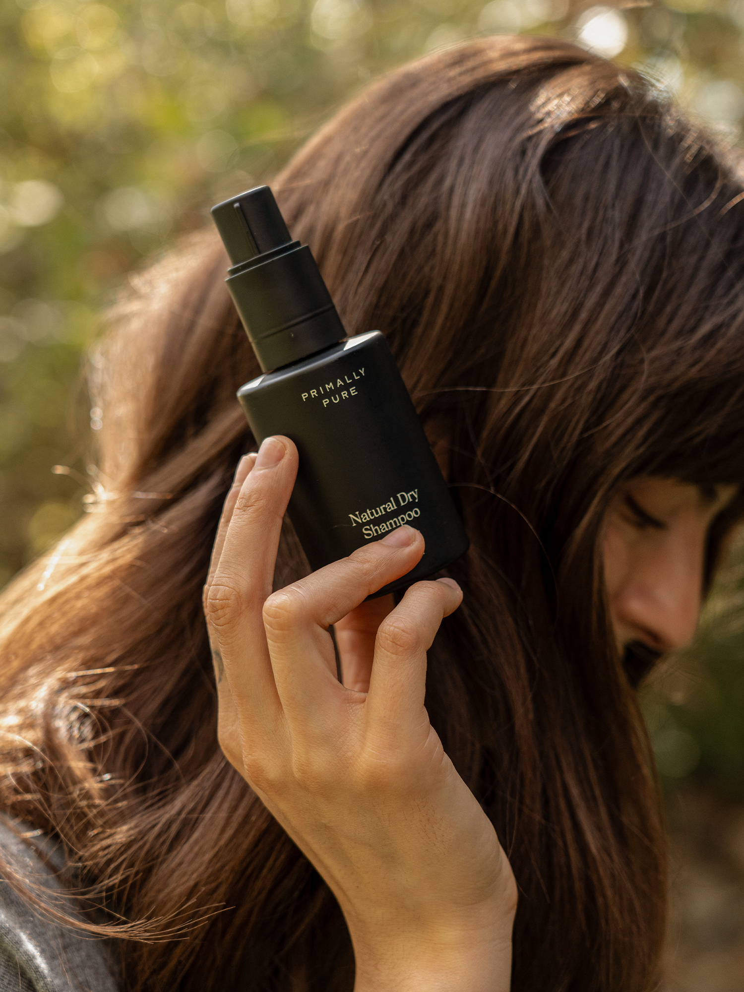 Person holding Primally Pure Natural Dry Shampoo in a black bottle, designed for refreshing hair naturally.