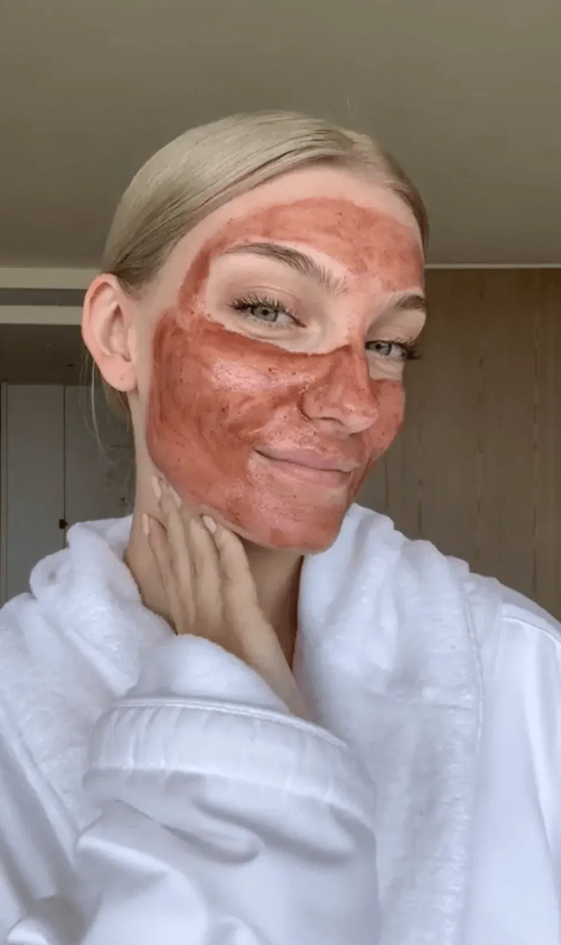 Woman with Primally Pure Plumping Face Mask applied to face wearing a white robe with a neutral background