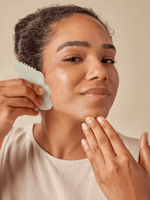 Person using a jade gua sha tool on their cheek with a relaxed expression.