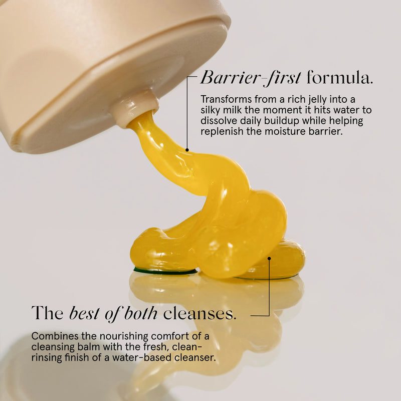 A close-up of Primally Pure Jelly to Milk cleansing balm being squeezed from a beige primally pure cleanser bottle onto a reflective white surface. Black text callouts describe the product formula and benefits.