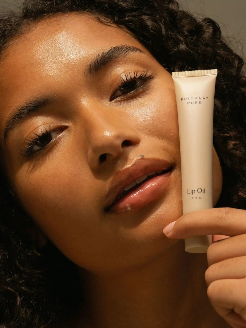 Primally Pure Lip Oil being held by model and applied to lips