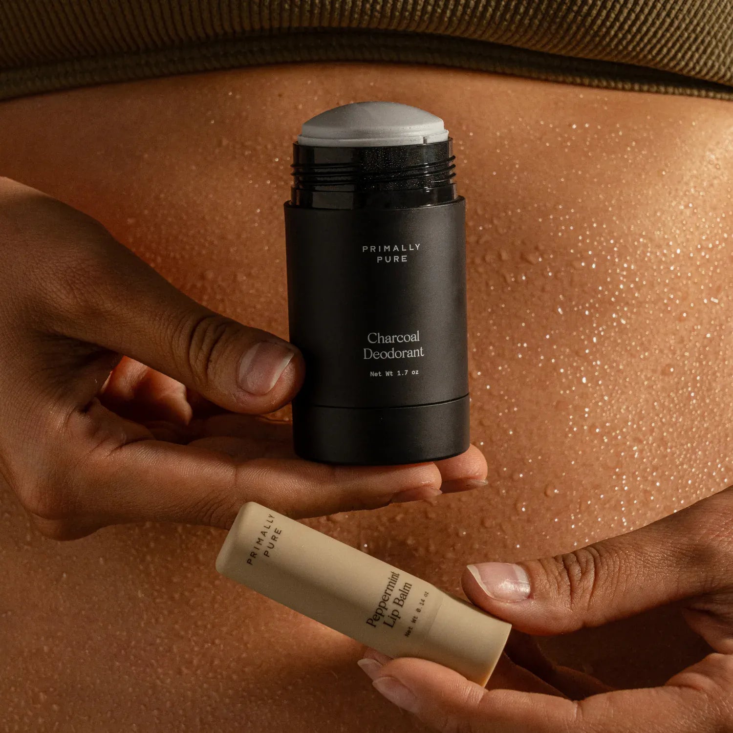 A person holds a Primally Pure Charcoal Deodorant stick in one hand and a Peppermint Puff Balm tube in the other. The Lips + Pits Duo Bundle 2 Best-Sellers at a bundled price