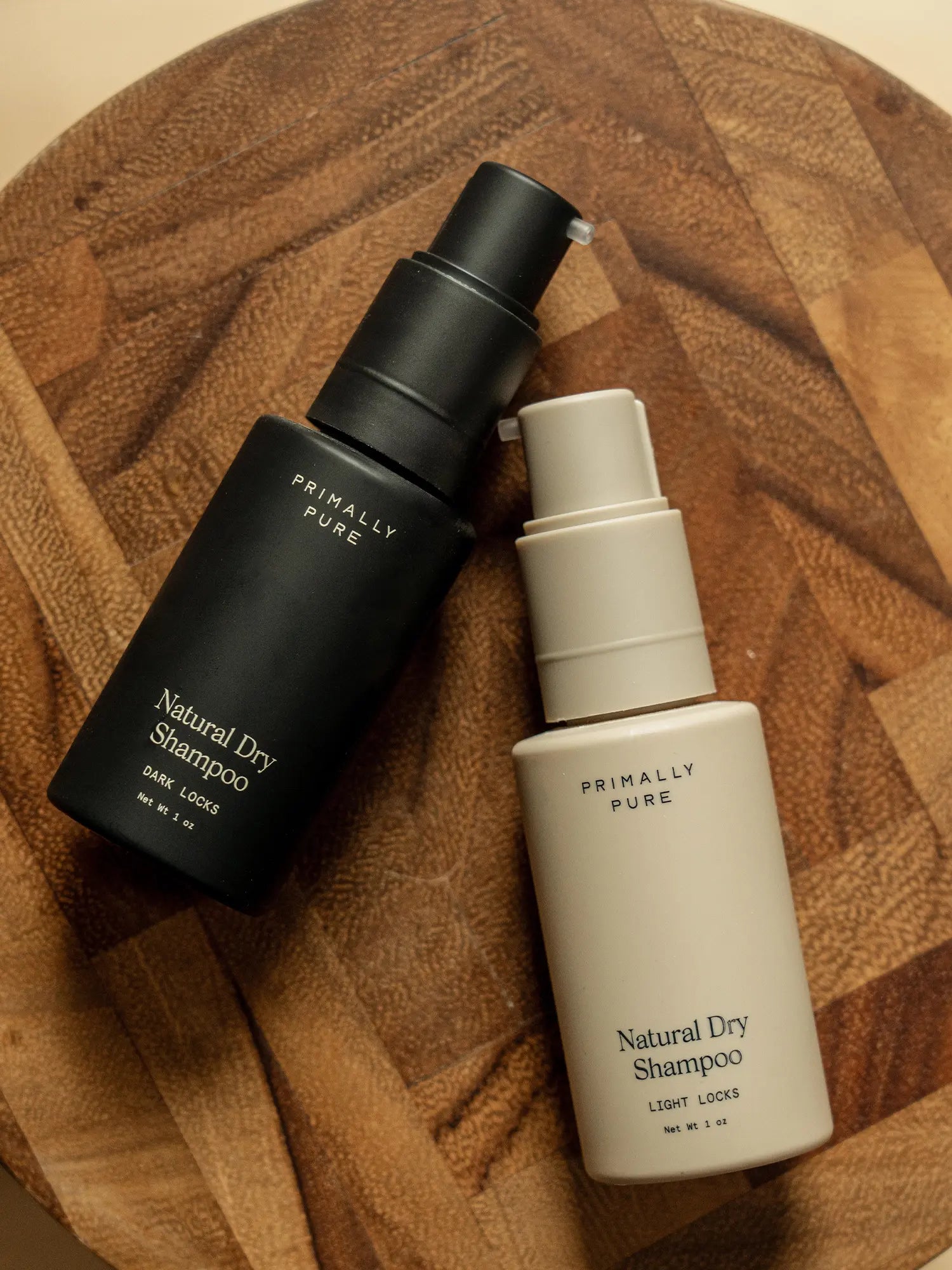 Primally Pure Natural Dry Shampoo bottles for dark and light locks displayed on a wooden surface.
