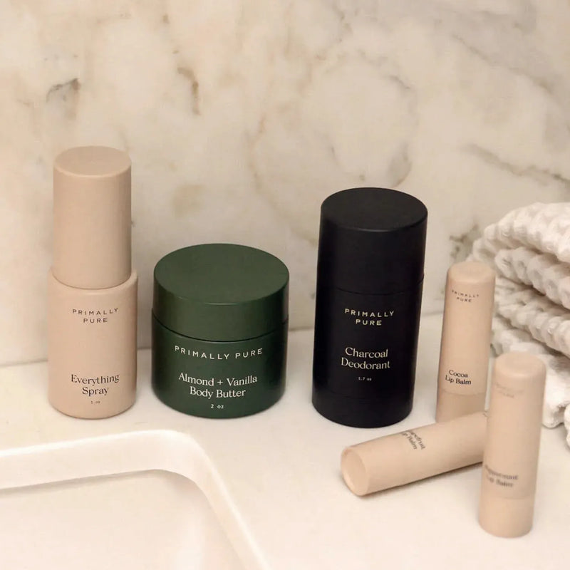 The Starter Kit Primally Pure skincare bundle arranged on a white marble surface, including a Everything Spray,  Almond + Vanilla Body Butter, Charcoal Deodorant, and three best-selling lip balms.