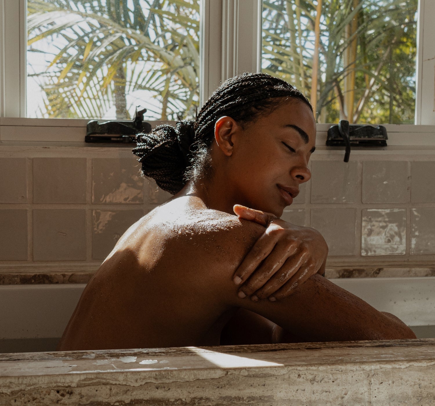 Woman sitting in a bathtub using Primally Pure Body Polish