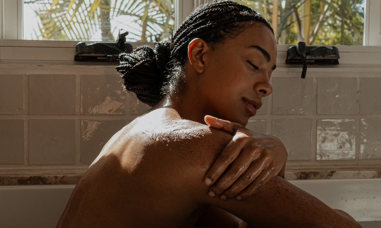 Woman sitting in a bathtub using Primally Pure Body Polish
